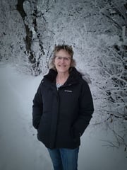 Kim Martin in winter coat standing outdoors with snow on the ground and trees behind