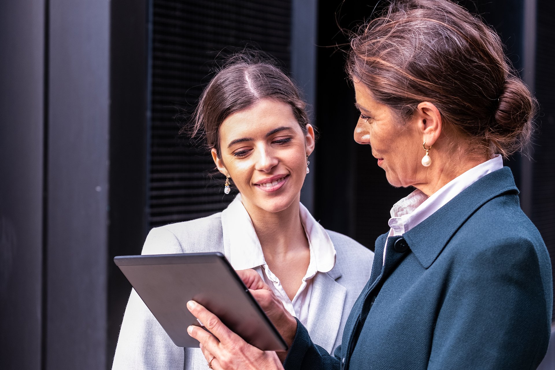 Professionally dressed young woman and mature woman looking at a tablet.