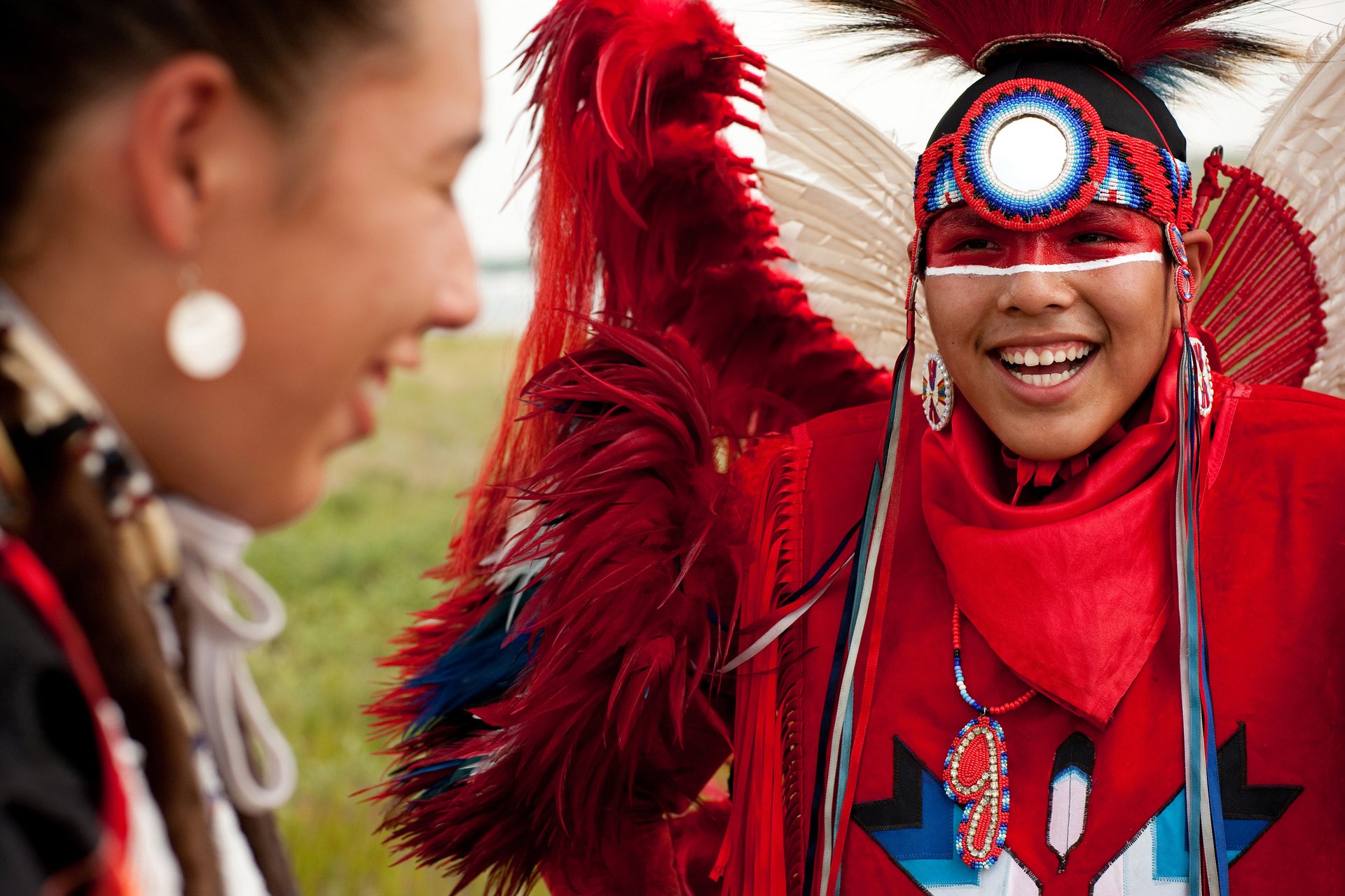 Indigenous woman dressed in regalia smiling at Indigenous man