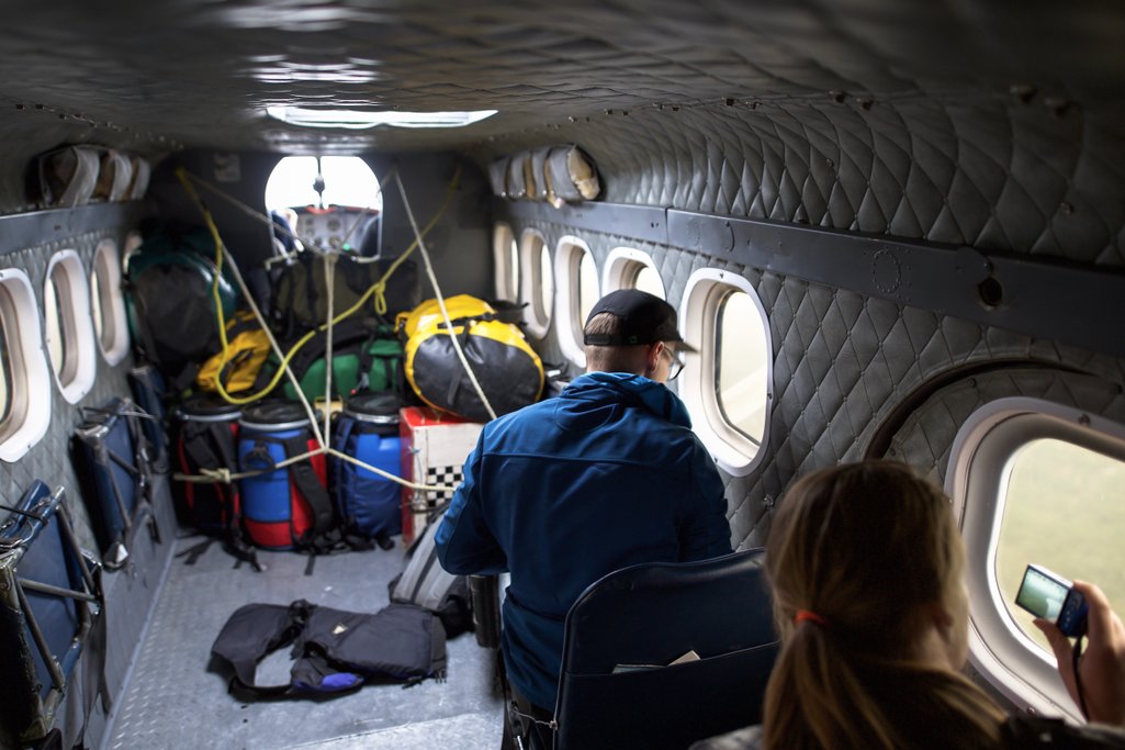 View inside of small plane with canoe and camping gear and two people looking out the windows.