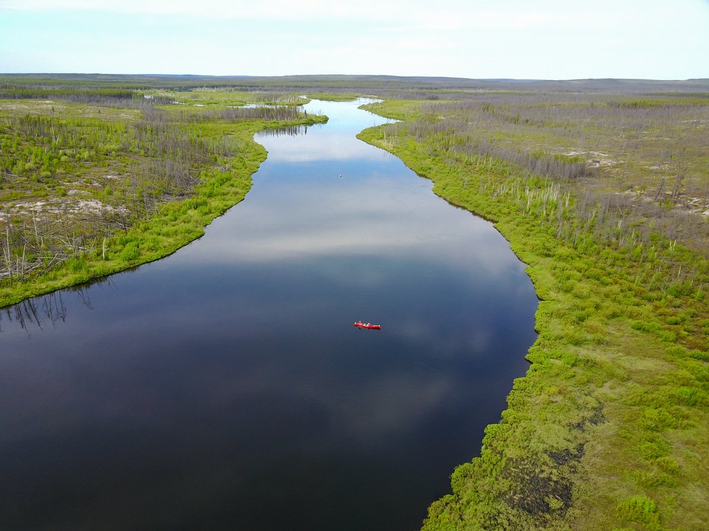 aerial view of a red canoe on a large river surrounded by dense forest in northern saskatchewan