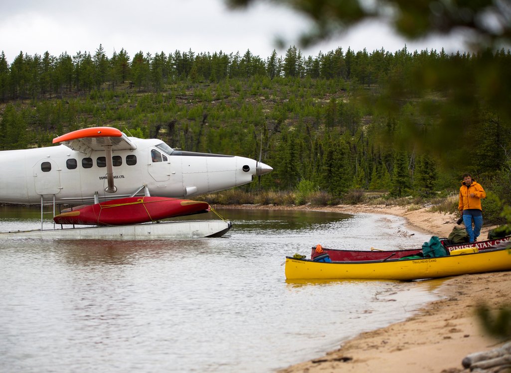 picture of a float plane on the water in front of a sandy beach surrounded by northern saskatchewan forest