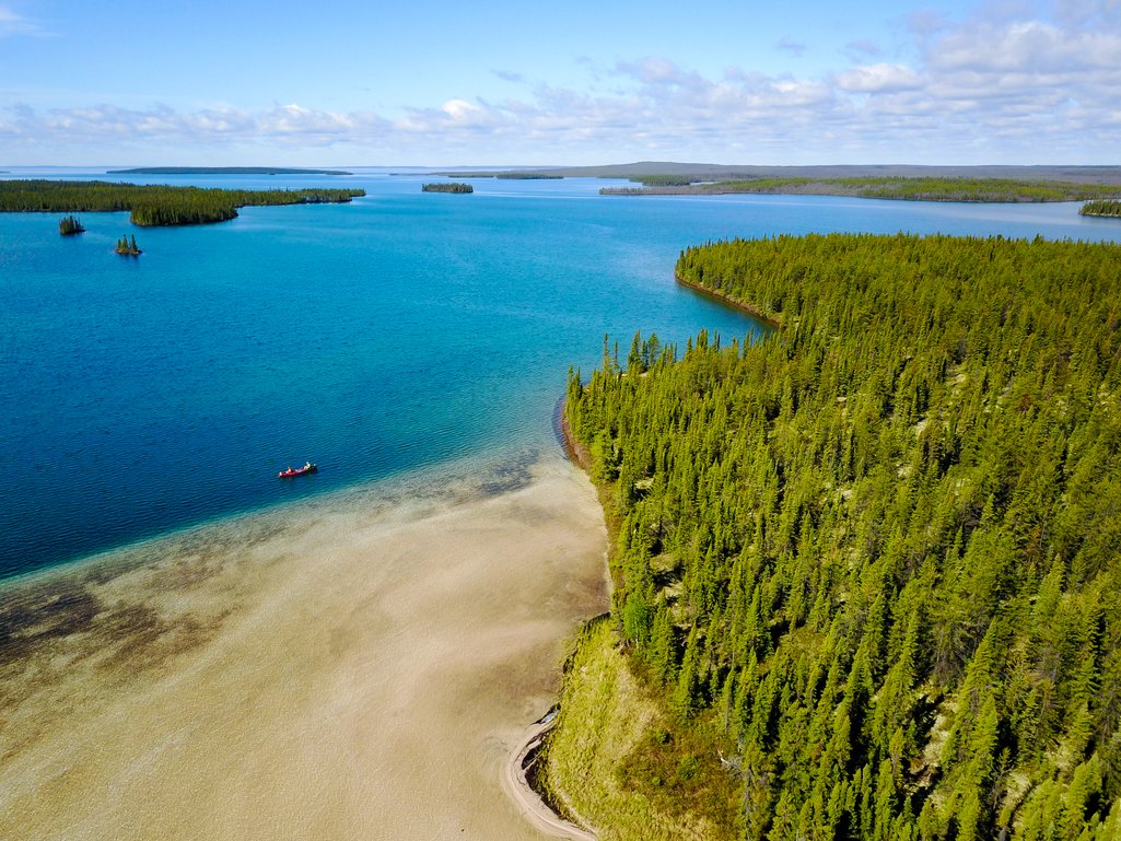 aerial view of a bright blue river in northern saskatchewan with dense forest and a sandy beach