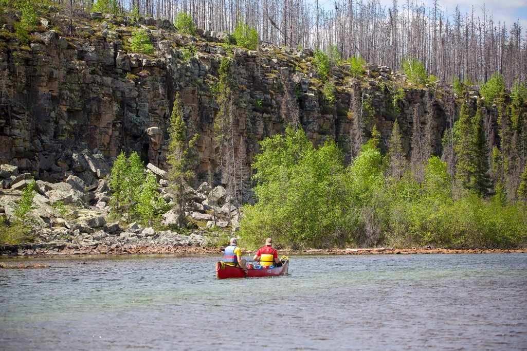 two people in a canoe on a river beside a tall cliff that looks to be crumbling