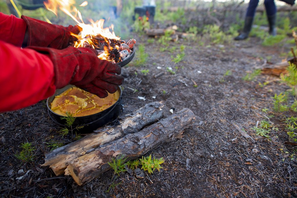 fire glove protected hands holding a plate of burning coals that is cooking a cake in the wilderness of northern saskatchewan