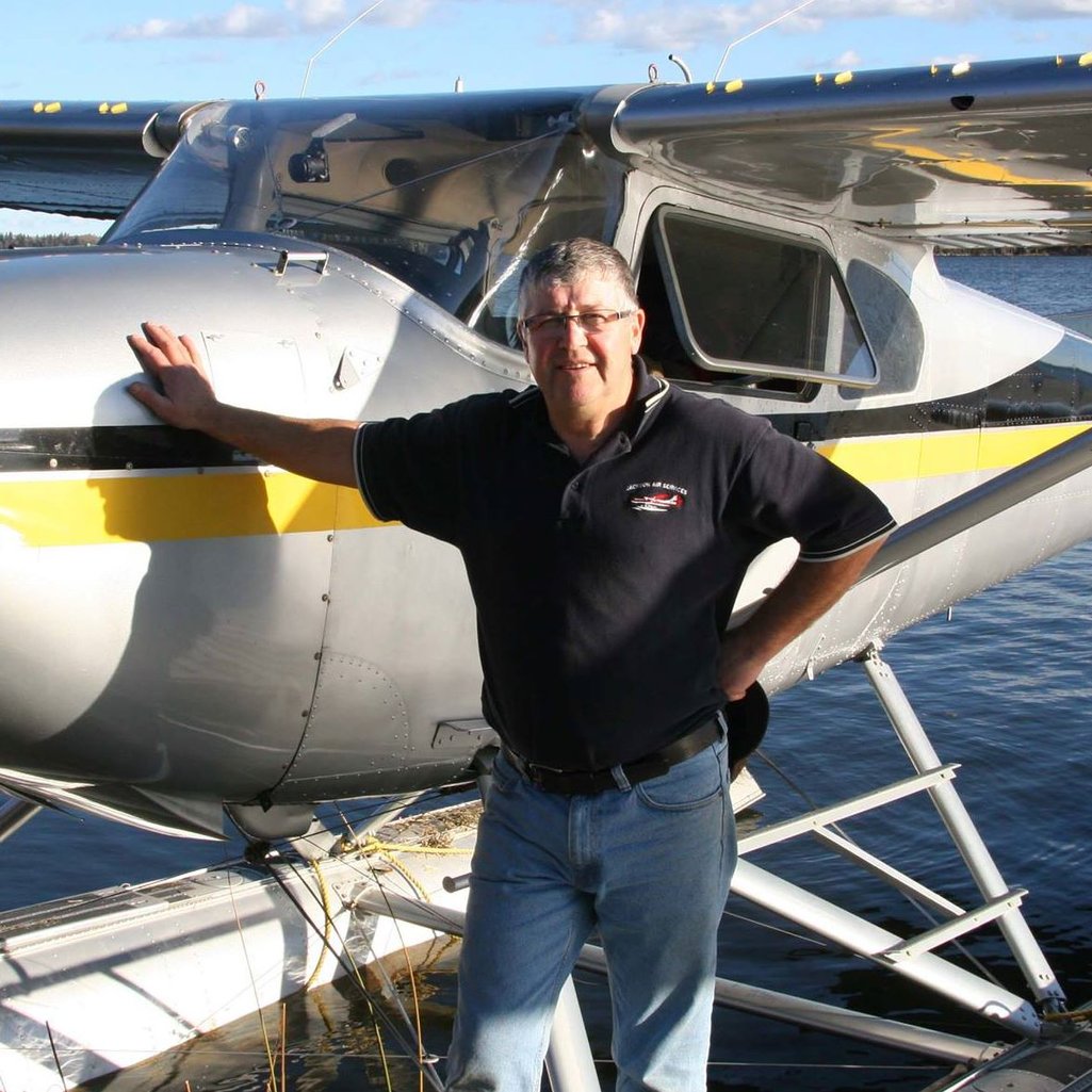 Person standing beside their float plane and touching it with their hand