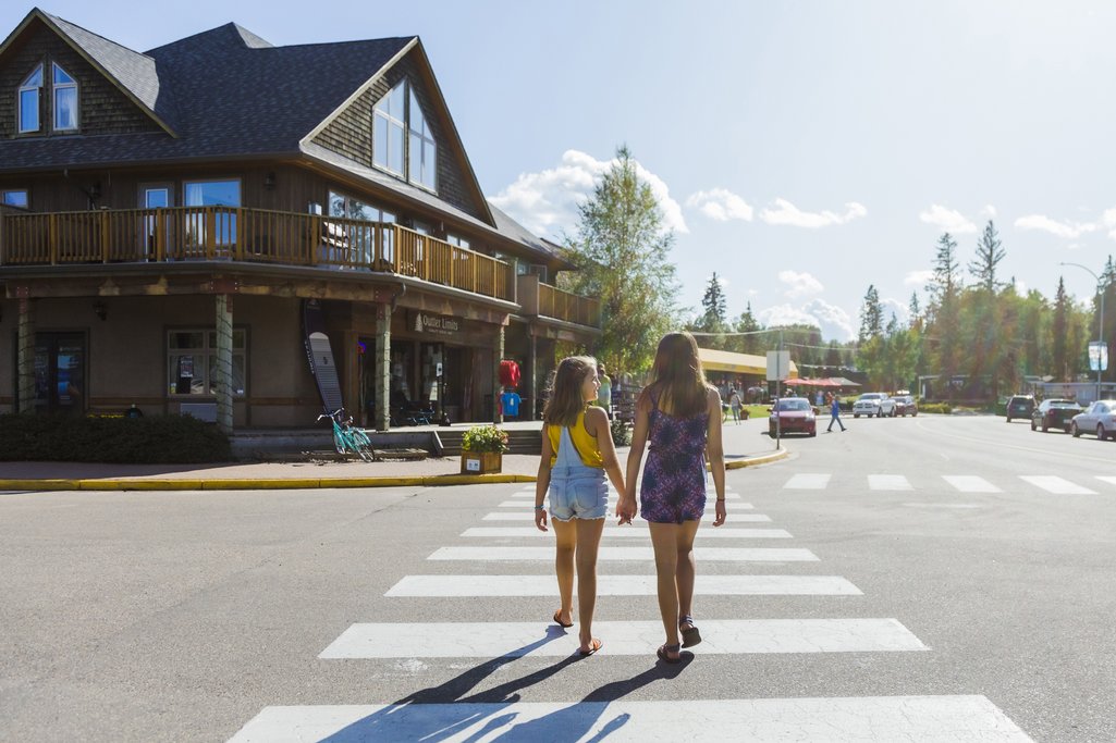 two young kids holding hands and crossing the road on a sunny day in Waskesiu