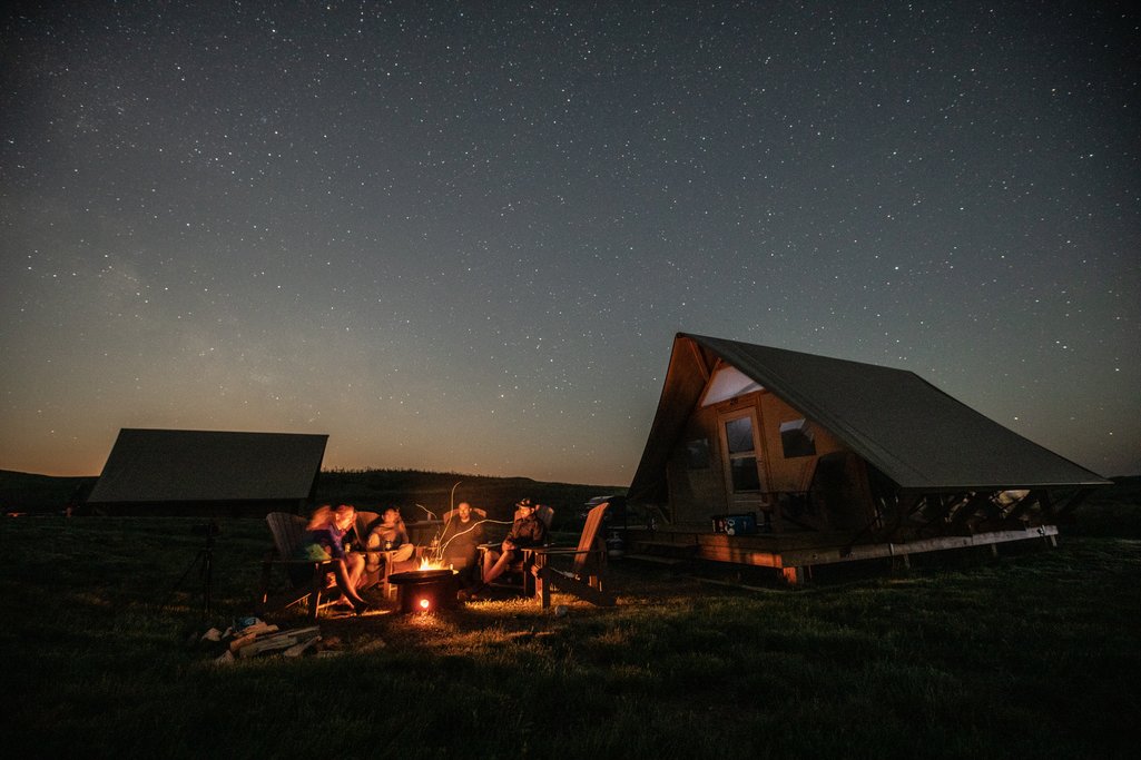 Group sitting around a fire at night with a clear sky and stars above them beside a Parks Canada oTENTik tent.
