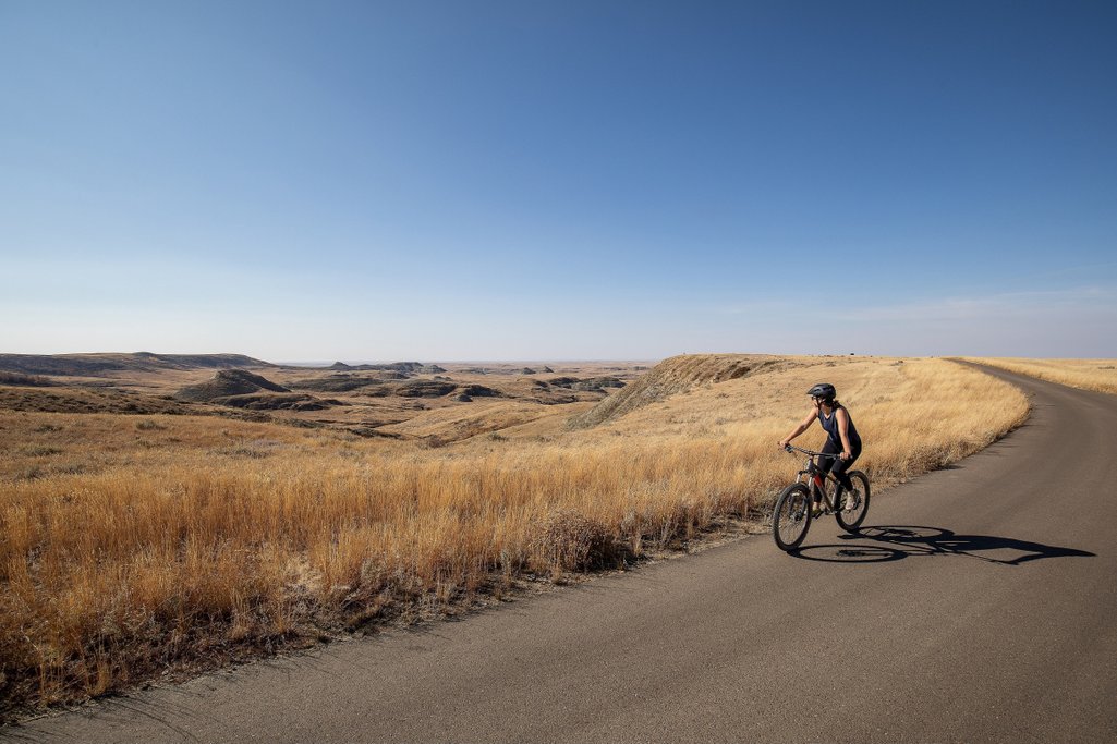Person biking along the Badlands Parkway in Grasslands National Park on a blue sky summer day