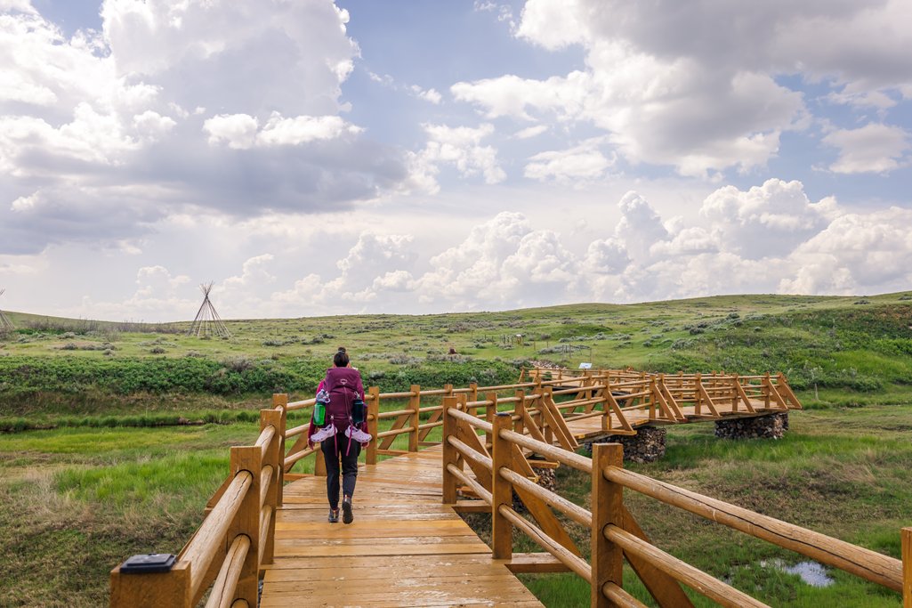 person with large backpack on walking over bridge with green grasslands surrounding