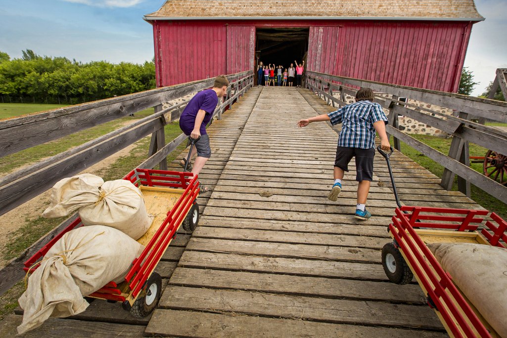 2 kids pulling wagons up a ramp towards a barn