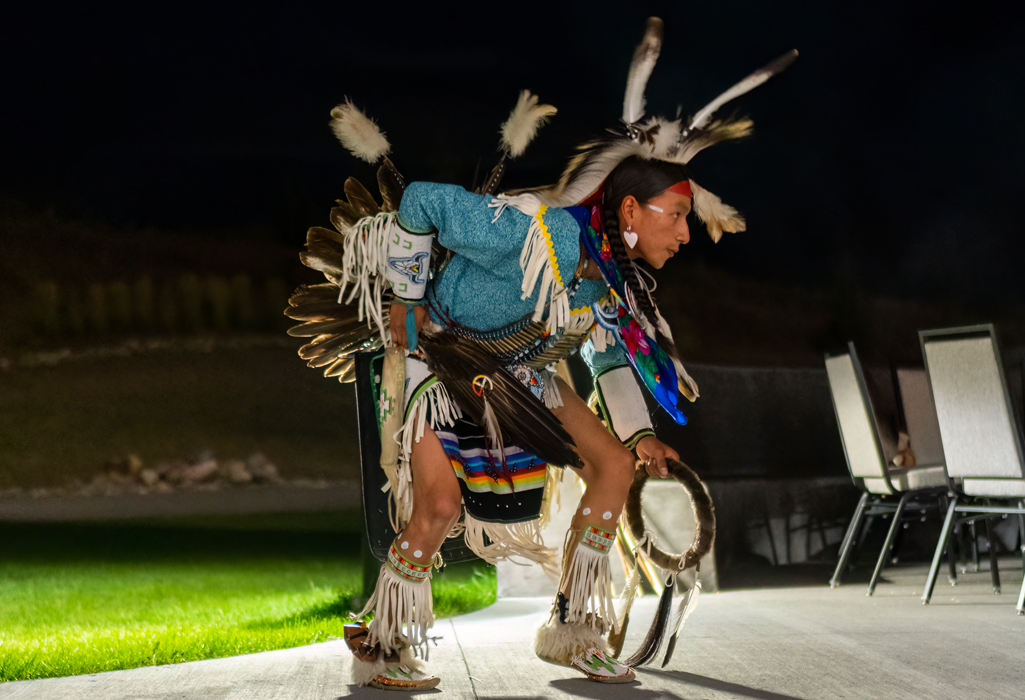 Indigenous dancer in traditional regalia performs at night outside Dakota Dunes Resort, celebrating Dakota culture through song and movement.