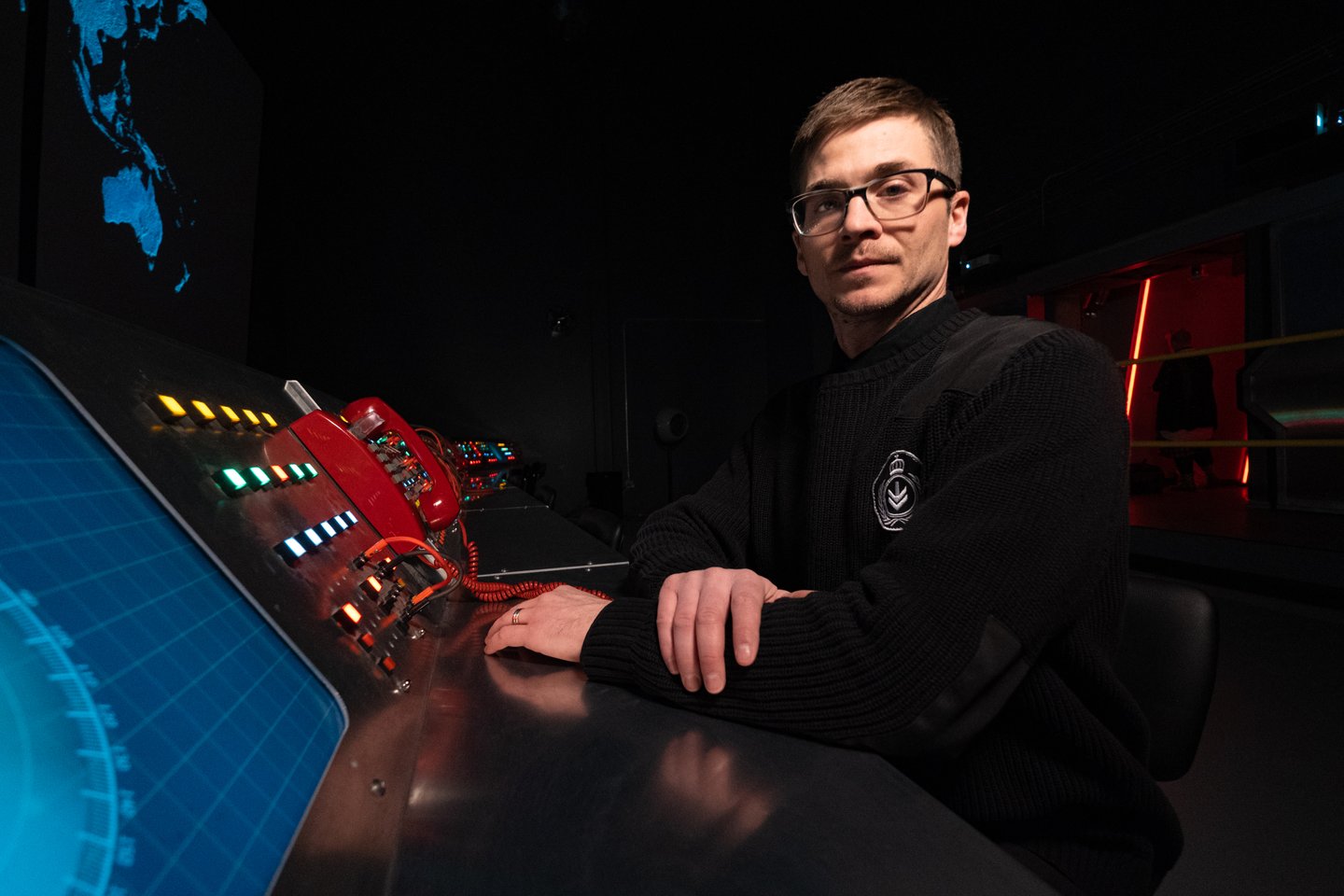Guide dressed in a naval uniform inside the Tunnels of Moose Jaw attraction in Saskatchewan, standing at a control station with red phones and glowing radar screens.