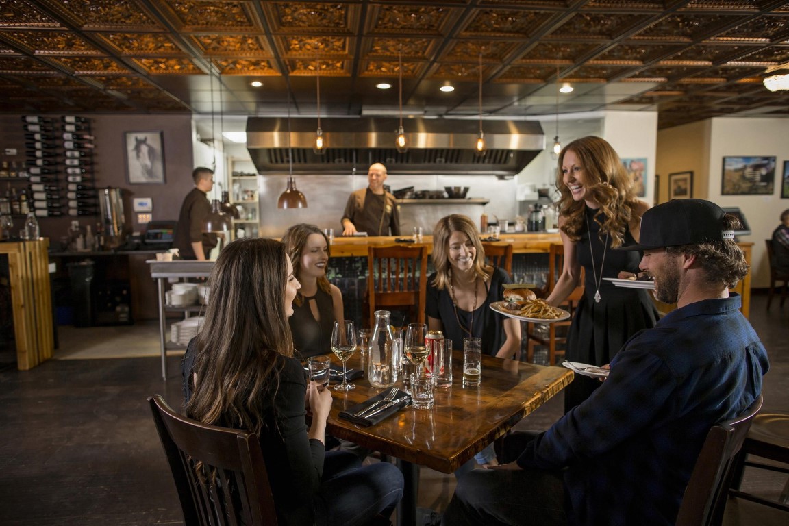 A cheerful server delivering a meal to a group of friends dining at a warmly lit restaurant