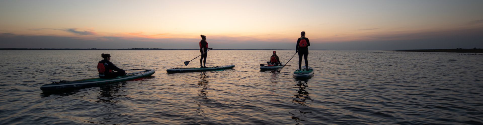 stand up paddleboarders on a lake at sunset.