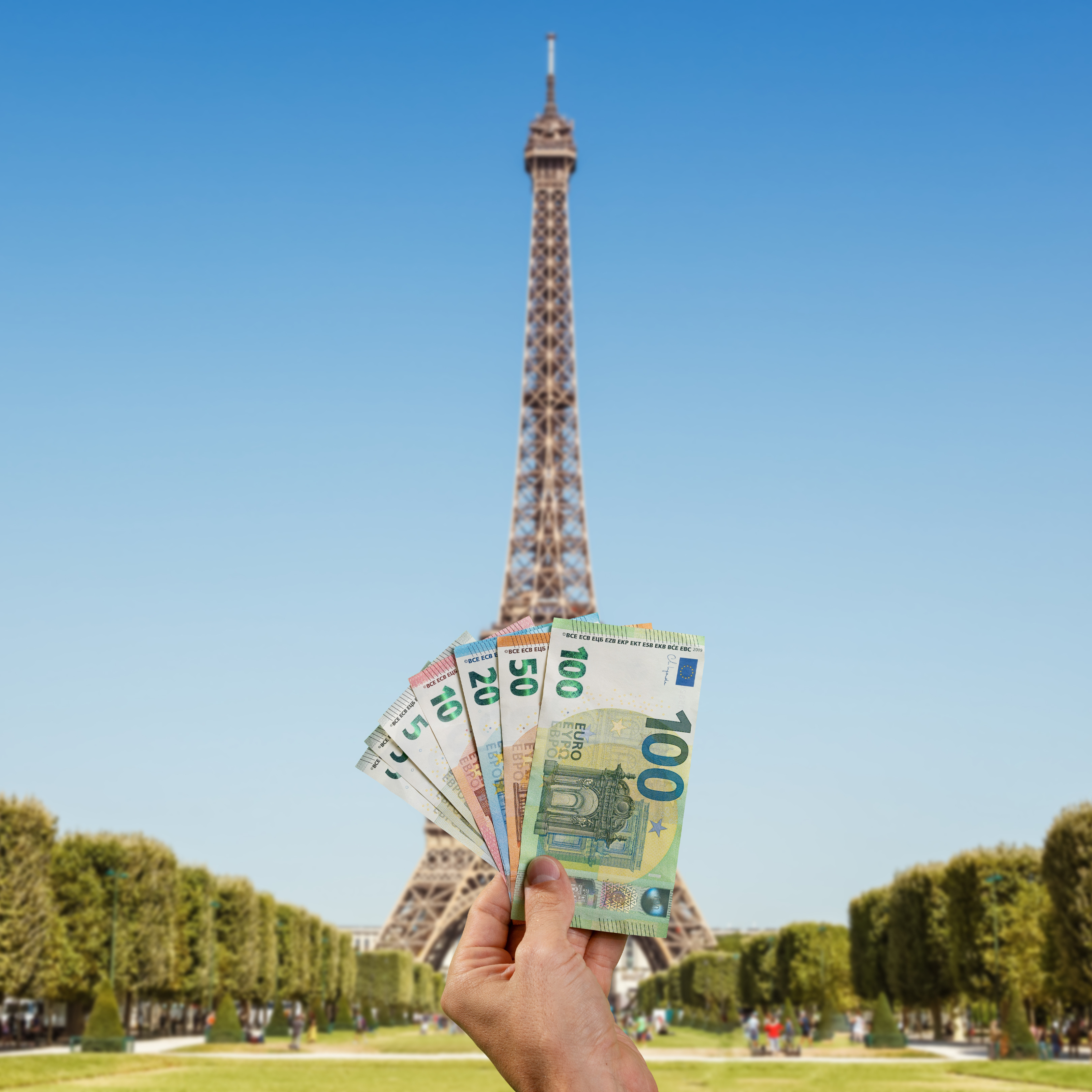 Traveller holding Euro (EUR) currency in front of Eiffel Tower in Paris, France