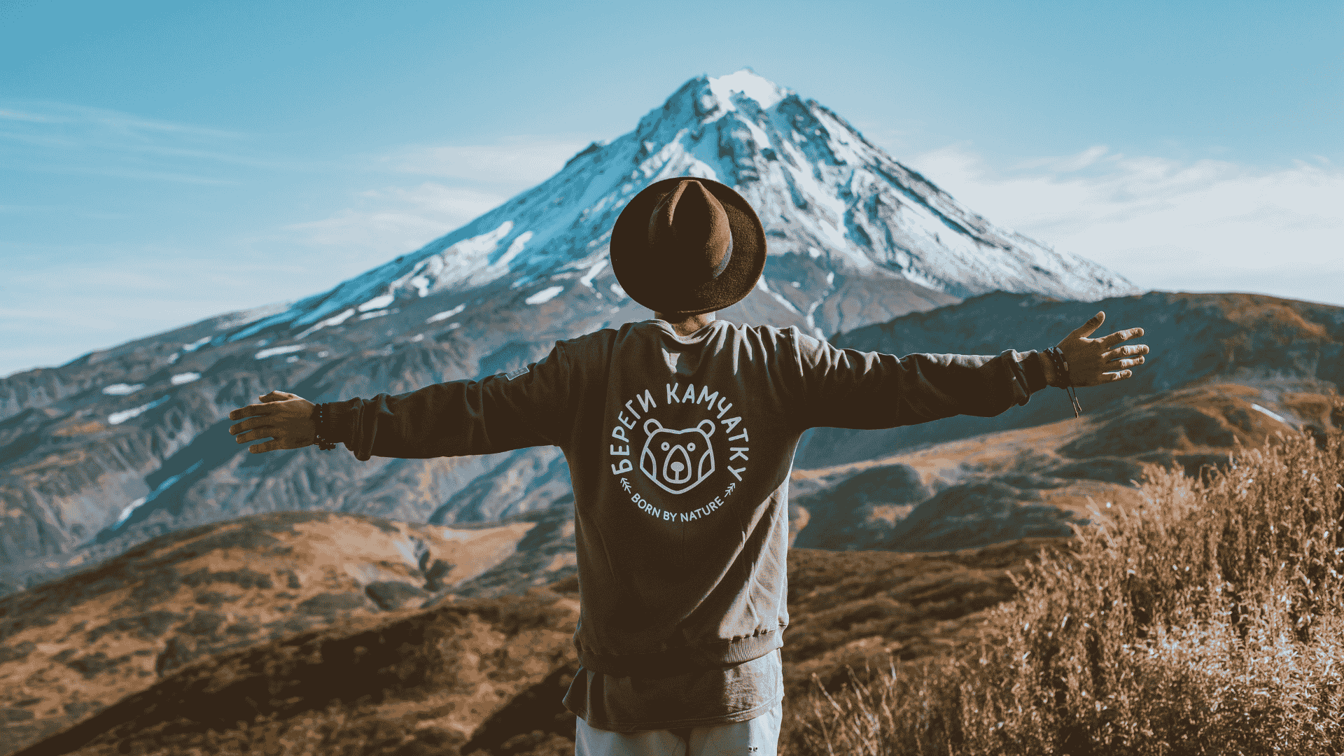 Solo Male Traveller with arms wide open in front of snowy mountain.