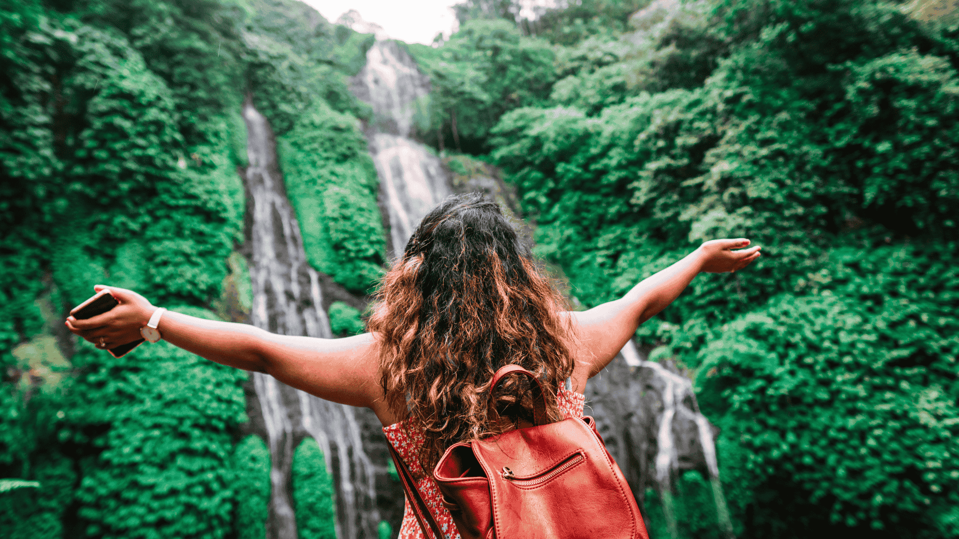 Solo Female Traveller with arms wide open in front of waterfall.