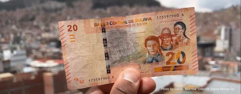 Daniel Mamba Odoi holding up a Bolivian Boliviano note to the Bolivian skyline while travelling South America