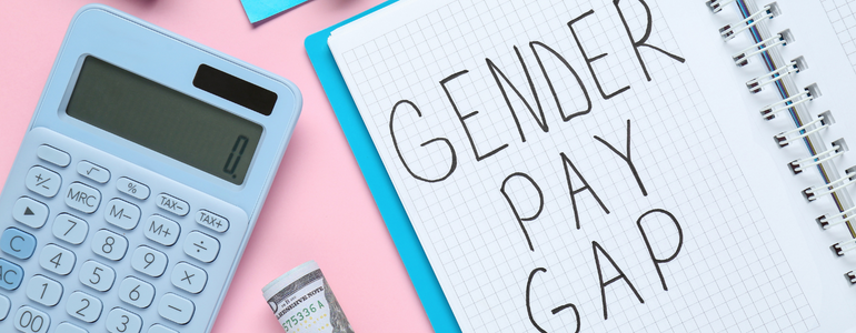 The Gender Pay Gap; written on a notepad, next to a calculator, on a pink and blue background. The Gender Pay Gap; written on a notepad, next to a calculator, on a pink and blue background.