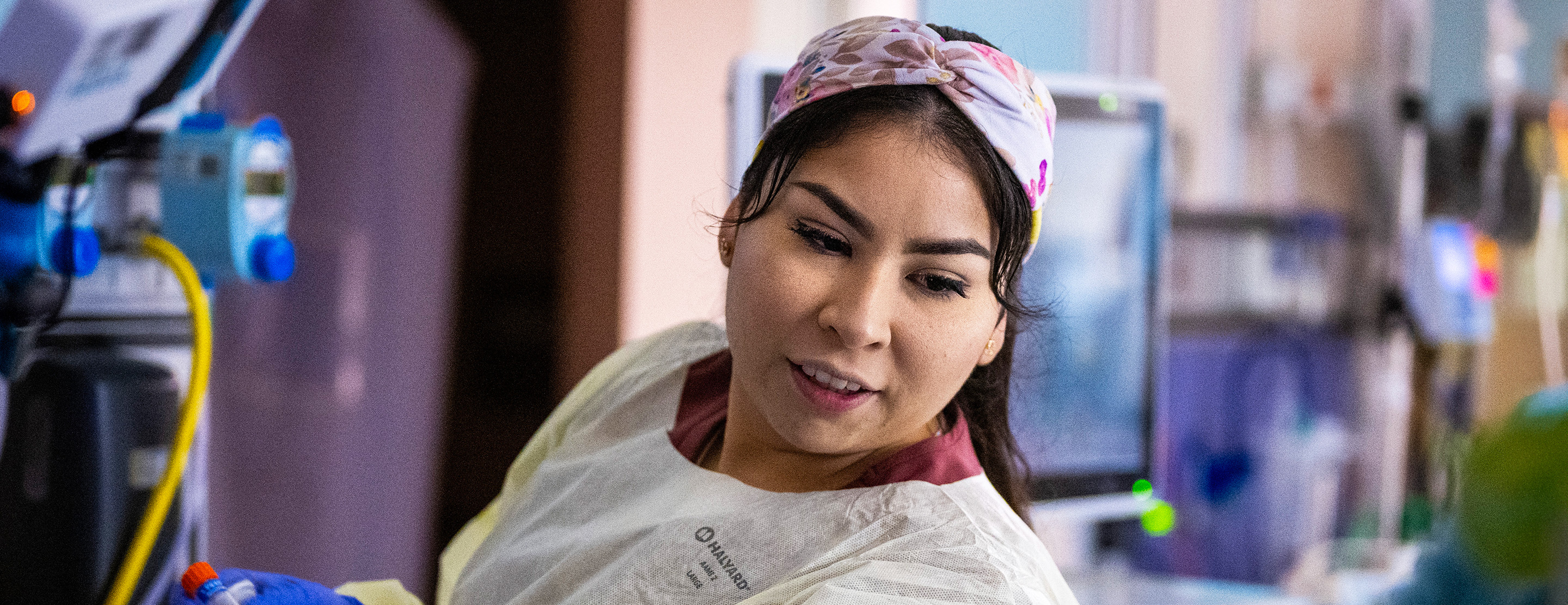 Nurse Roxana Gonzalez, in a floral head wrap and protective gown, tends to a patient in the neonatal intensive care unit.