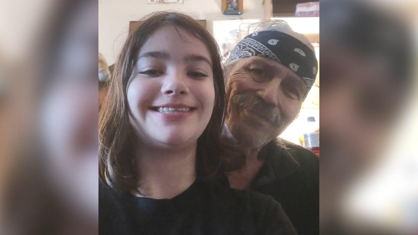 A smiling teenage girl takes a selfie with an older man wearing a bandana