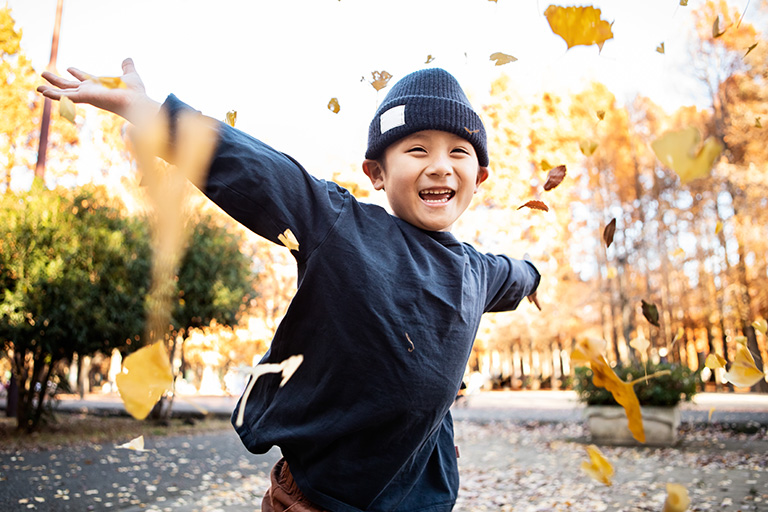 Happy child playing in the park during autumn, with leaves falling around them and smiling on a sunny afternoon.