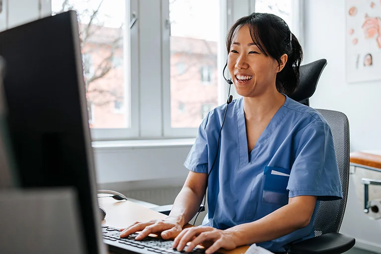 Smiling woman using a laptop in a well-lit environment with plants around her.