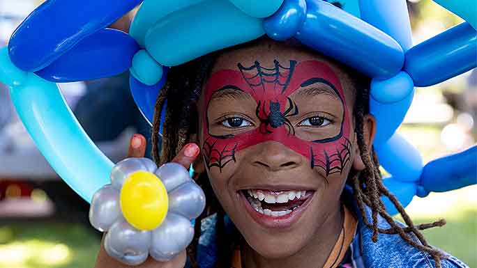 Smiling girl wearing spidery face paint and large balloon hat