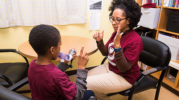 Registered nurse Syrennia McArthur Hanshaw helps a student use his inhaler in the school-based asthma program
