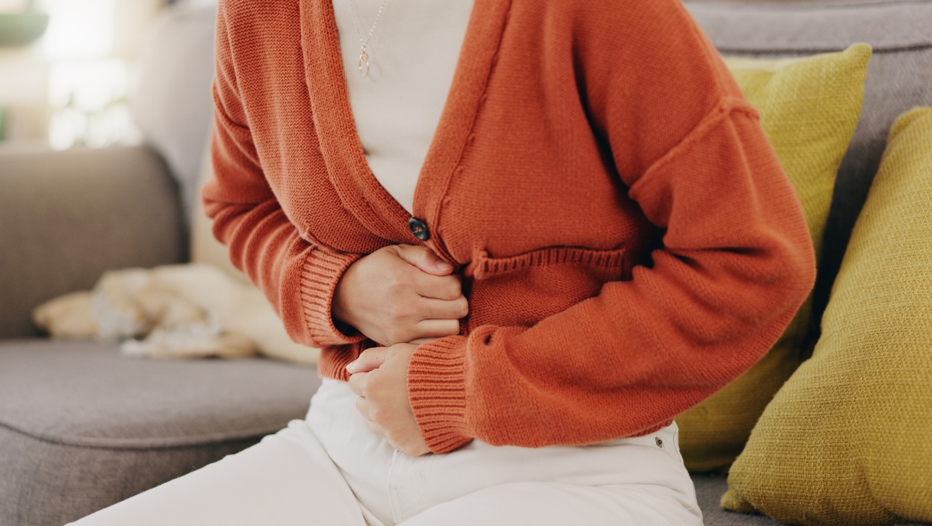 person in orange sweater clutching abdomin in pain