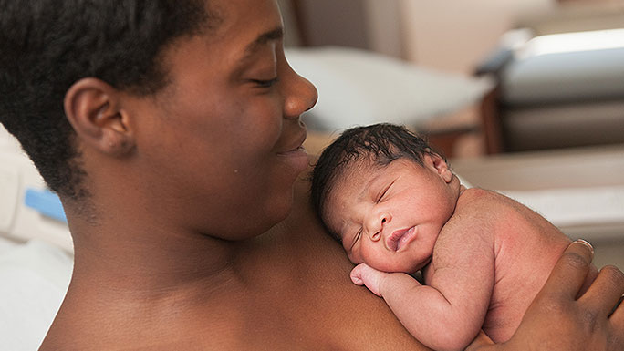 Smiling mom cradles newborn skin-to-skin