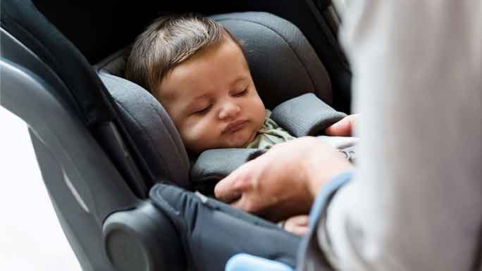 Hands buckling baby into car seat