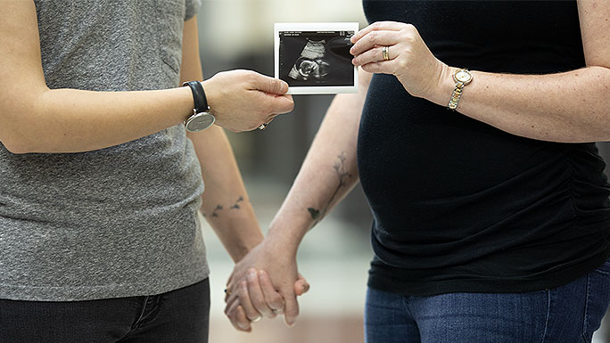 Pregnant lesbian couple holding hands, zoomed in on baby bump and sonogram