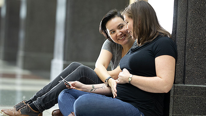 Lesbian couple smiling at sonogram and cupping pregnant belly