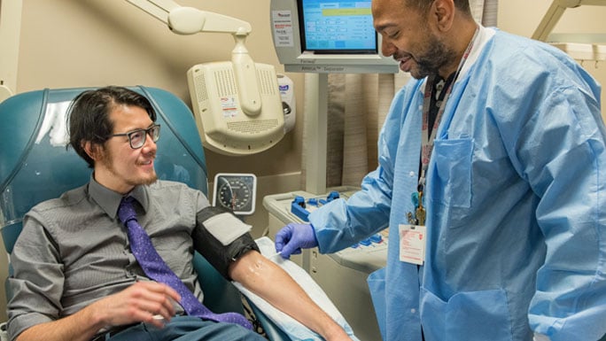 Pathologist Chancey Christensen, MD, seated, prepares to donate platelets in the blood donation clinic. Technician Terrance Collier, standing