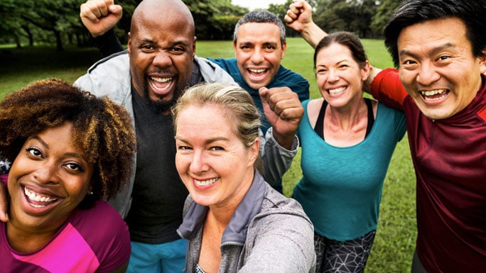 group of adults in active wear standing in a grassy park setting