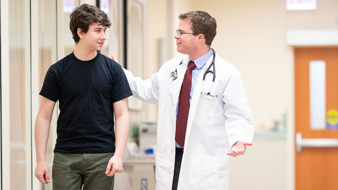 Image of Dr. Mark Applebaum, MD, walking the hallway and talking to a pediatric cancer patient, Ari Volchenboum.