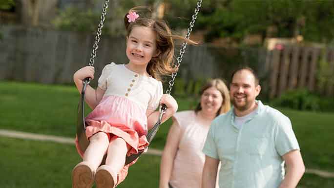 Pediatric leukemia survivor Joy Arseneau swings in the air while her parents watch and smile