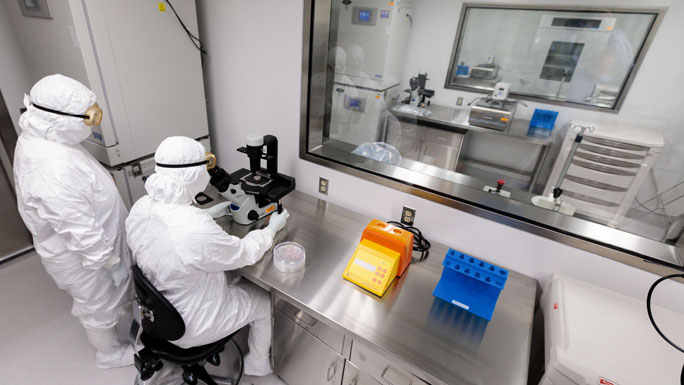 two lab workers in protective suits in Advanced Cellular Therapeutics Facility (ACTF)