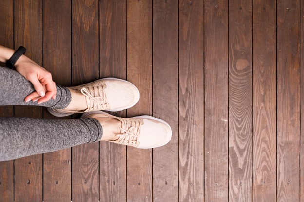 An overhead view of a person wearing sneakers on a wooden floor, representing healthy feet and ankles after successful treatment.  