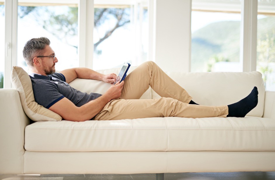 a man laying on a sofa looking at his tablet device