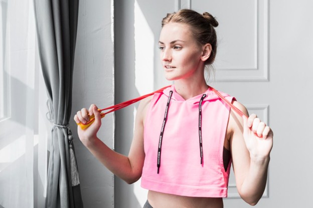 A young woman in a pink athletic top holding a jump rope, representing the positive outcome of overcoming muscle imbalance and poor conditioning.