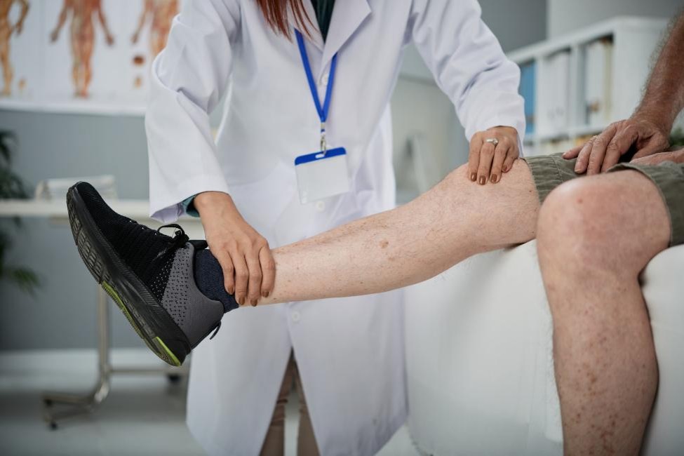 An orthopedic physician evaluating an adult patient’s leg during a musculoskeletal examination.