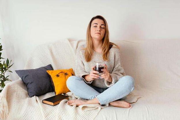 A woman sitting peacefully on a sofa drinking a cup of tea to promote comfort and digestive health.