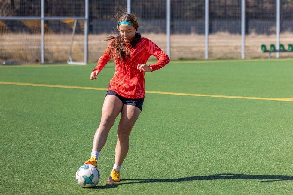 Teen soccer player stopping a ball during a practice session on a sports field.