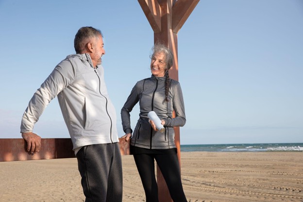 An active senior couple smiling on a beach in athletic wear representing the vitality supported by specialized GI services.