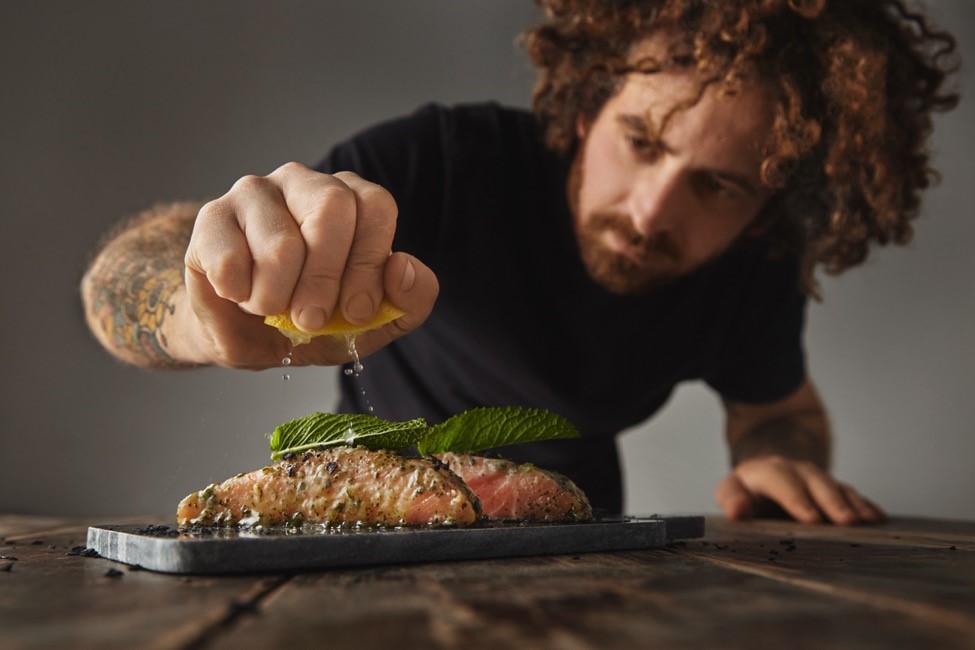 a man squeezes a lemon over a cooked fish.