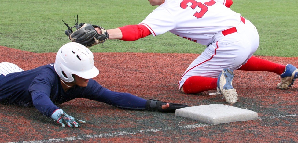 Teen baseball player stretching to reach a base before being tagged.