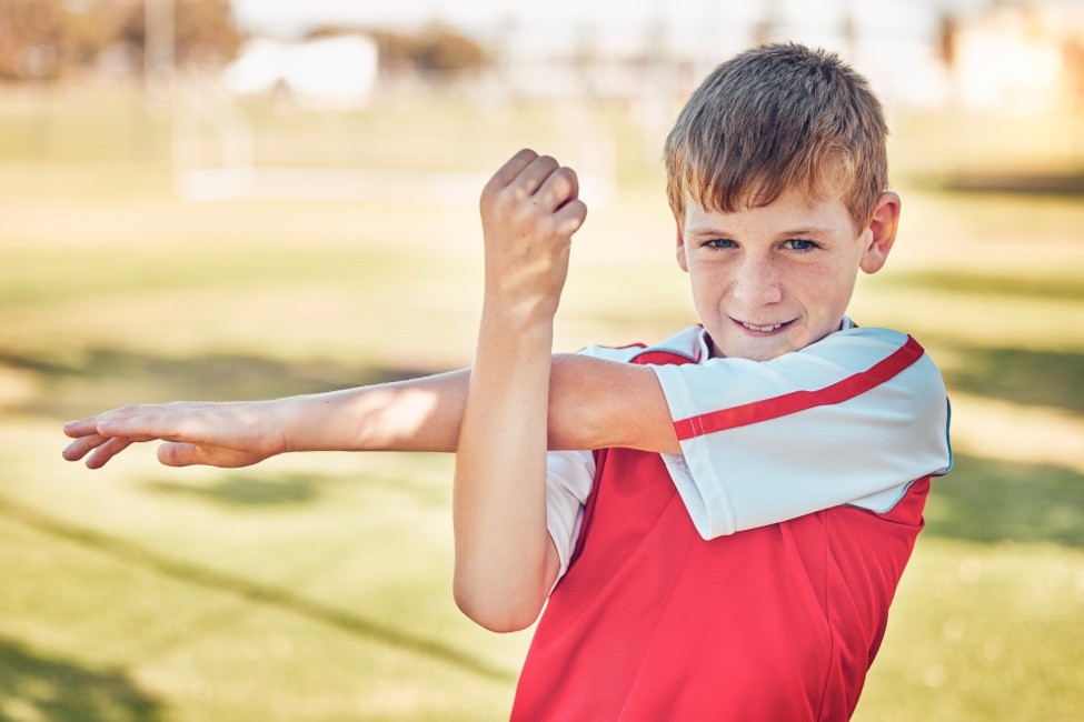 Teen athlete stretching his shoulder during a warm-up before sports practice.